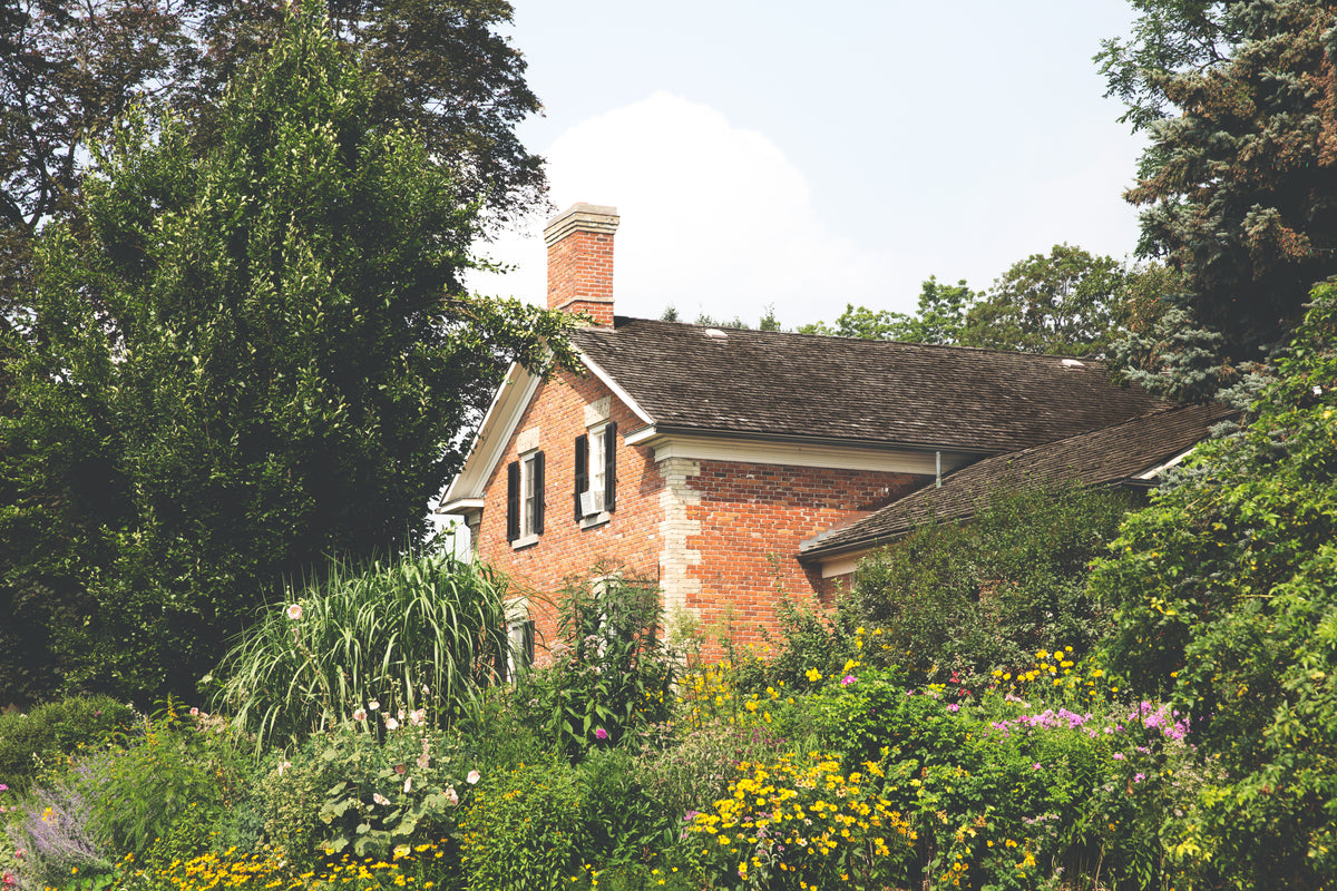 Brick country house surrounded by flowering garden beds and mature trees